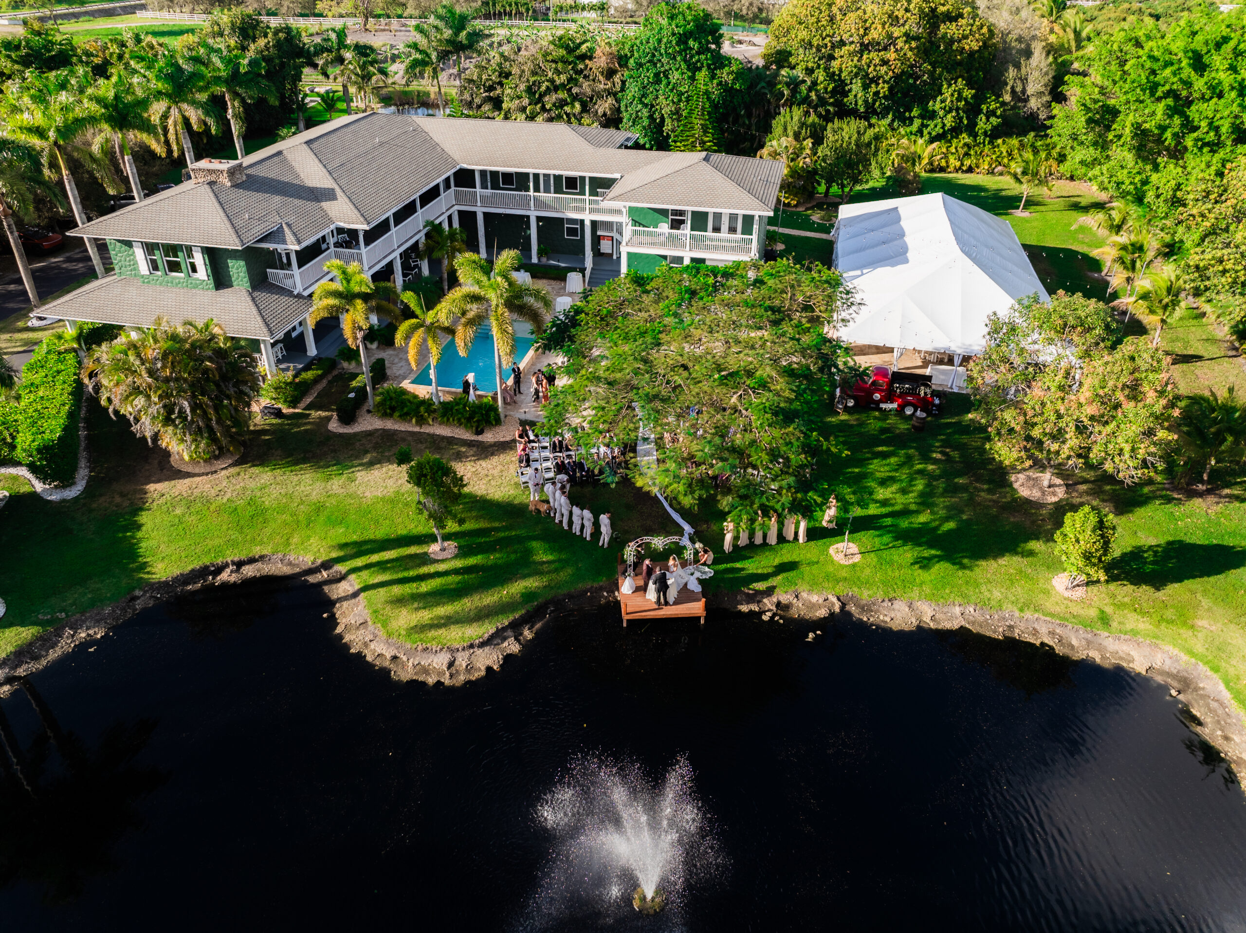 Aerial view of lakeside wedding ceremony and outdoor tent at Saint Patrick Palace in Davie, Florida.