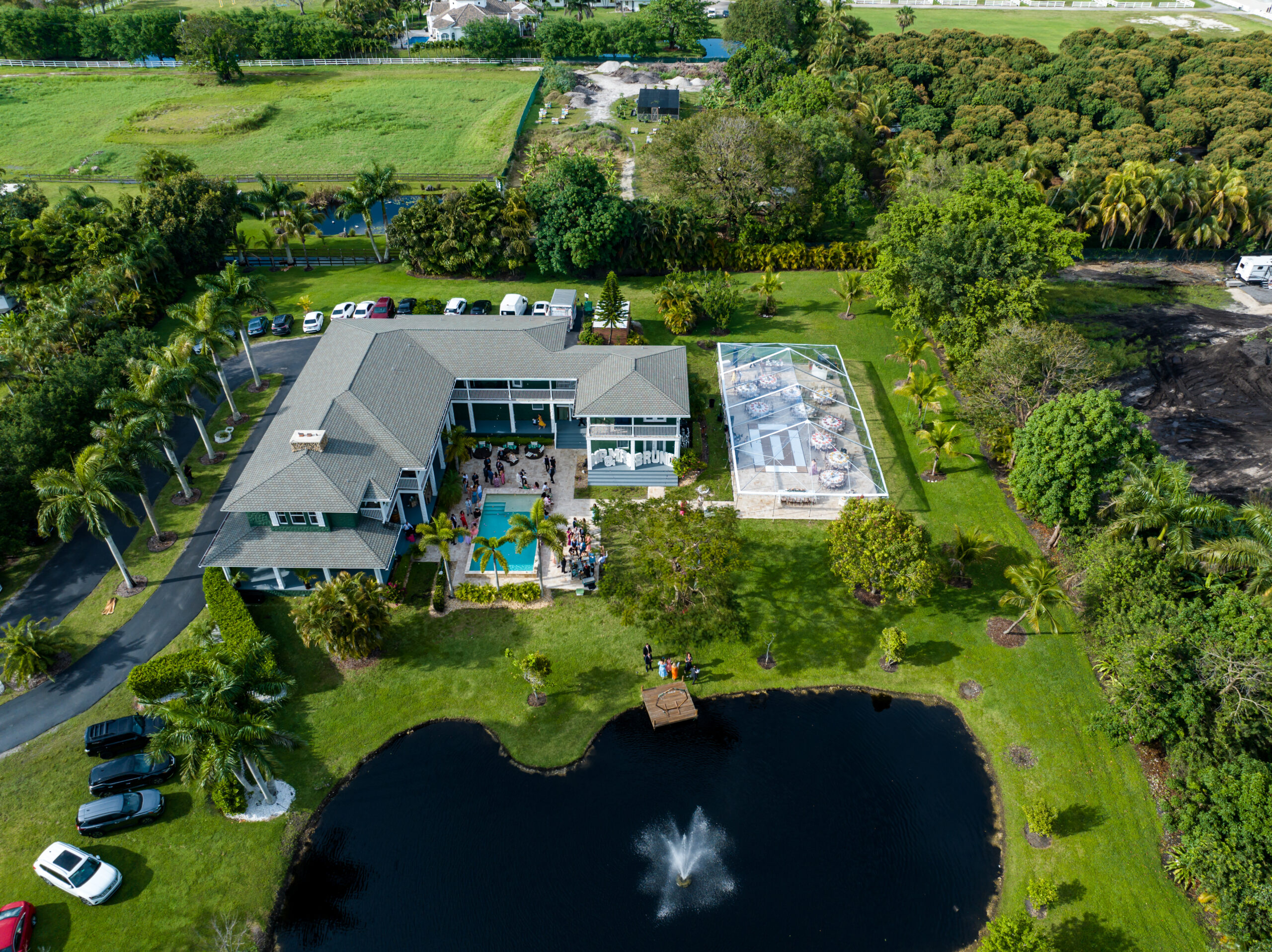Aerial view of luxury South Florida estate with lakeside wedding ceremony, reception tent, and fountain