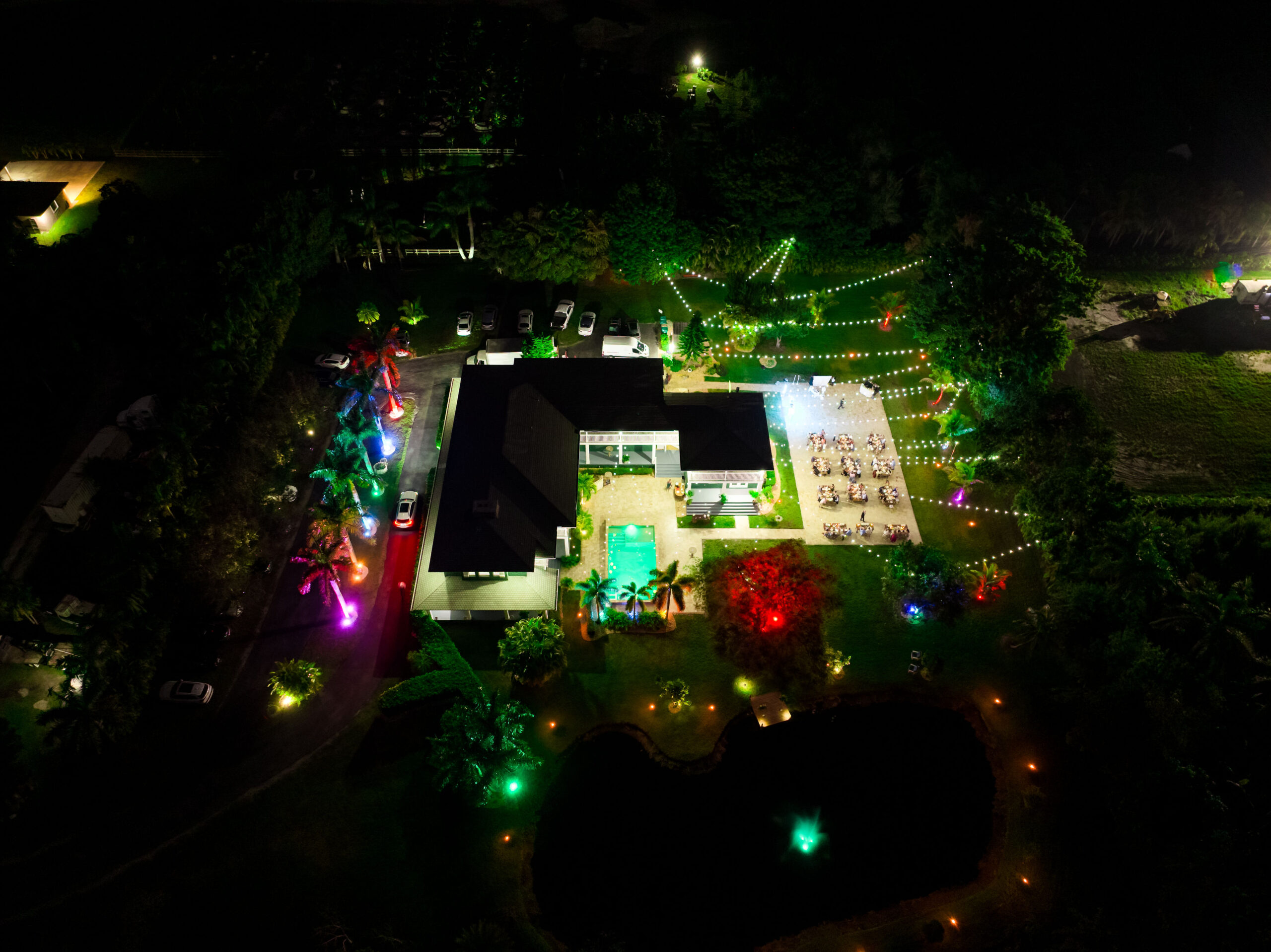 Nighttime aerial view of Saint Patrick Palace wedding estate with glowing lights and pool in Davie, Florida"